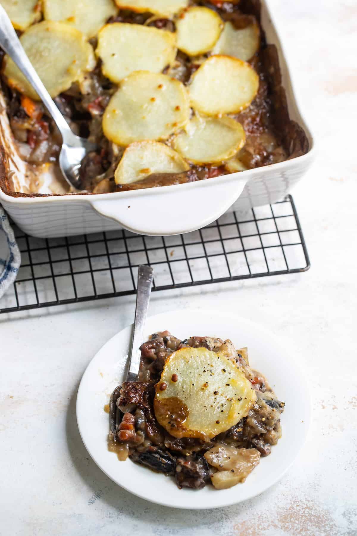 A Serving of Vegetable Moussaka on a Plate with a Pan of Moussaka Behind It