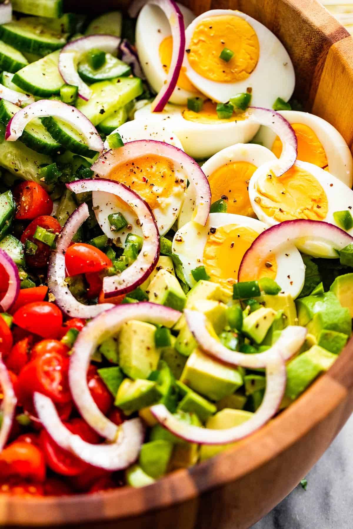 close up of sliced red onions, halved hard boiled eggs, chopped avocado, sliced cherry tomatoes, and sliced cucumbers