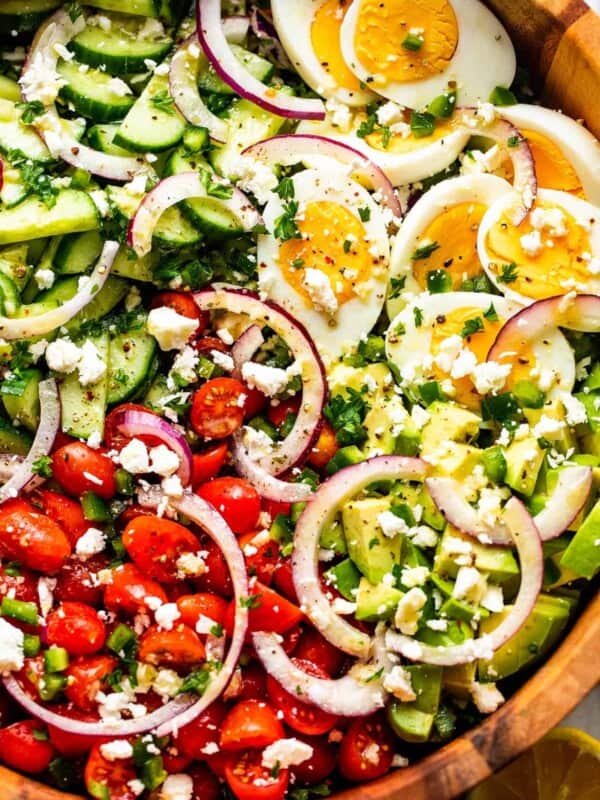 close up of sliced red onions, halved hard boiled eggs, chopped avocado, sliced cherry tomatoes, and sliced cucumbers topped with crumbled feta cheese