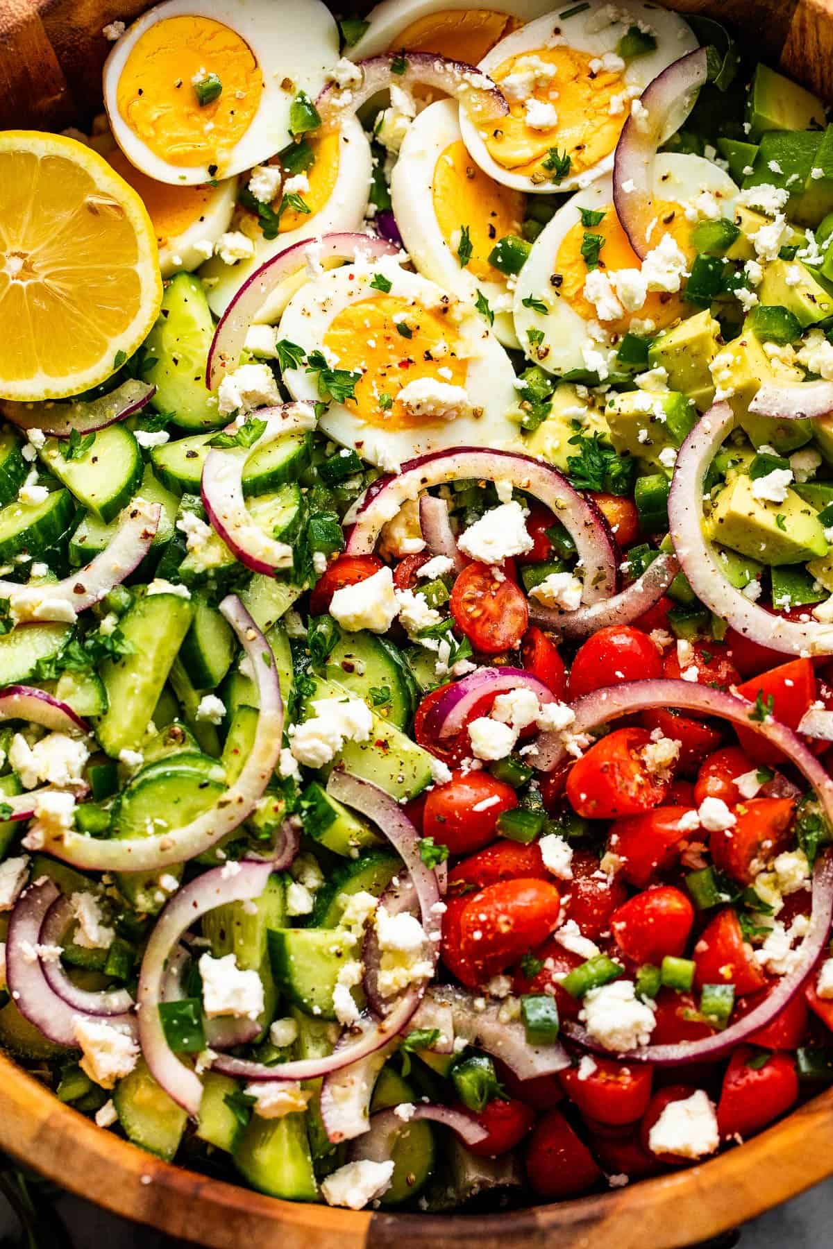 close up of sliced red onions, halved hard boiled eggs, chopped avocado, sliced cherry tomatoes, and sliced cucumbers