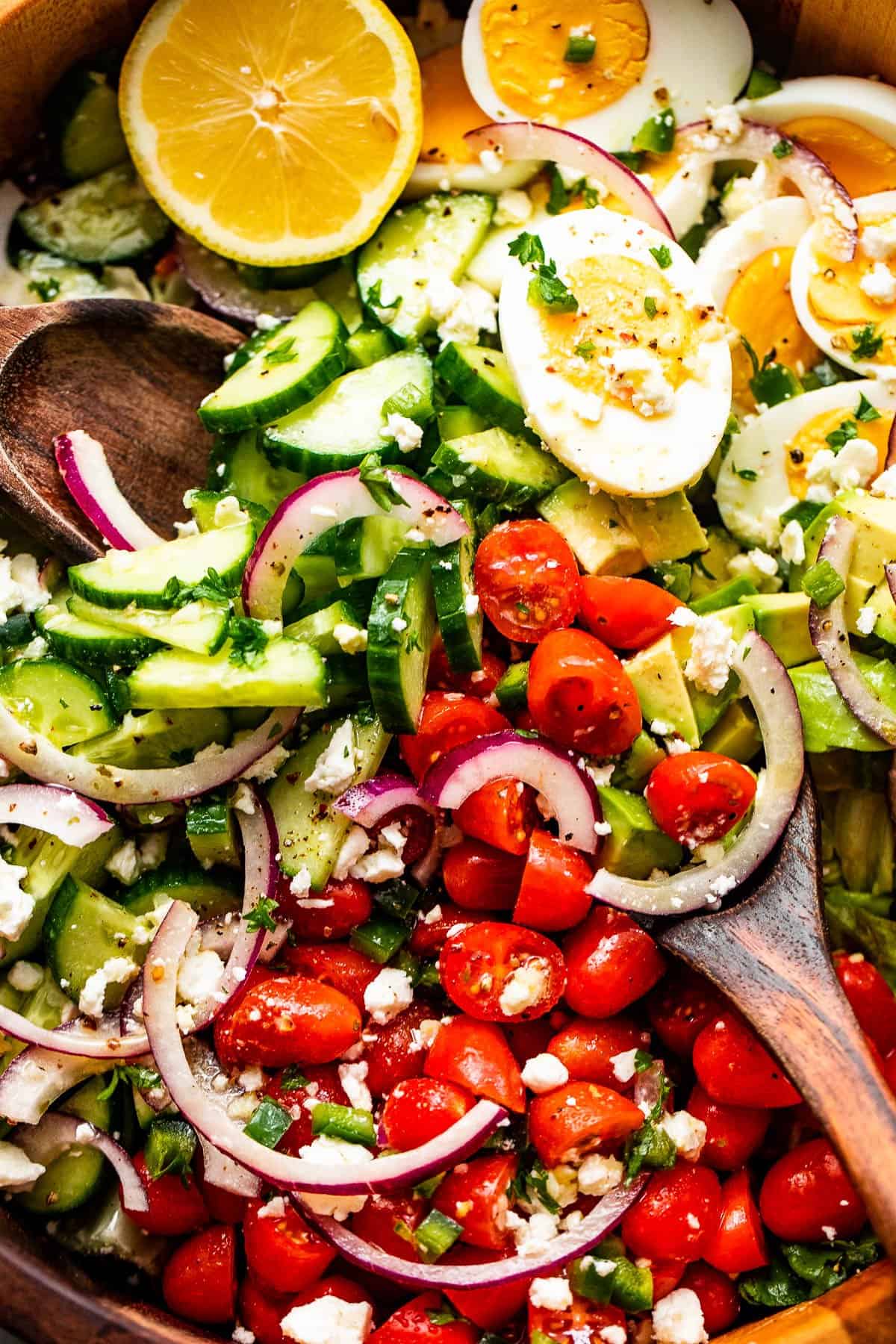 close up of sliced red onions, halved hard boiled eggs, chopped avocado, sliced cherry tomatoes, and sliced cucumbers