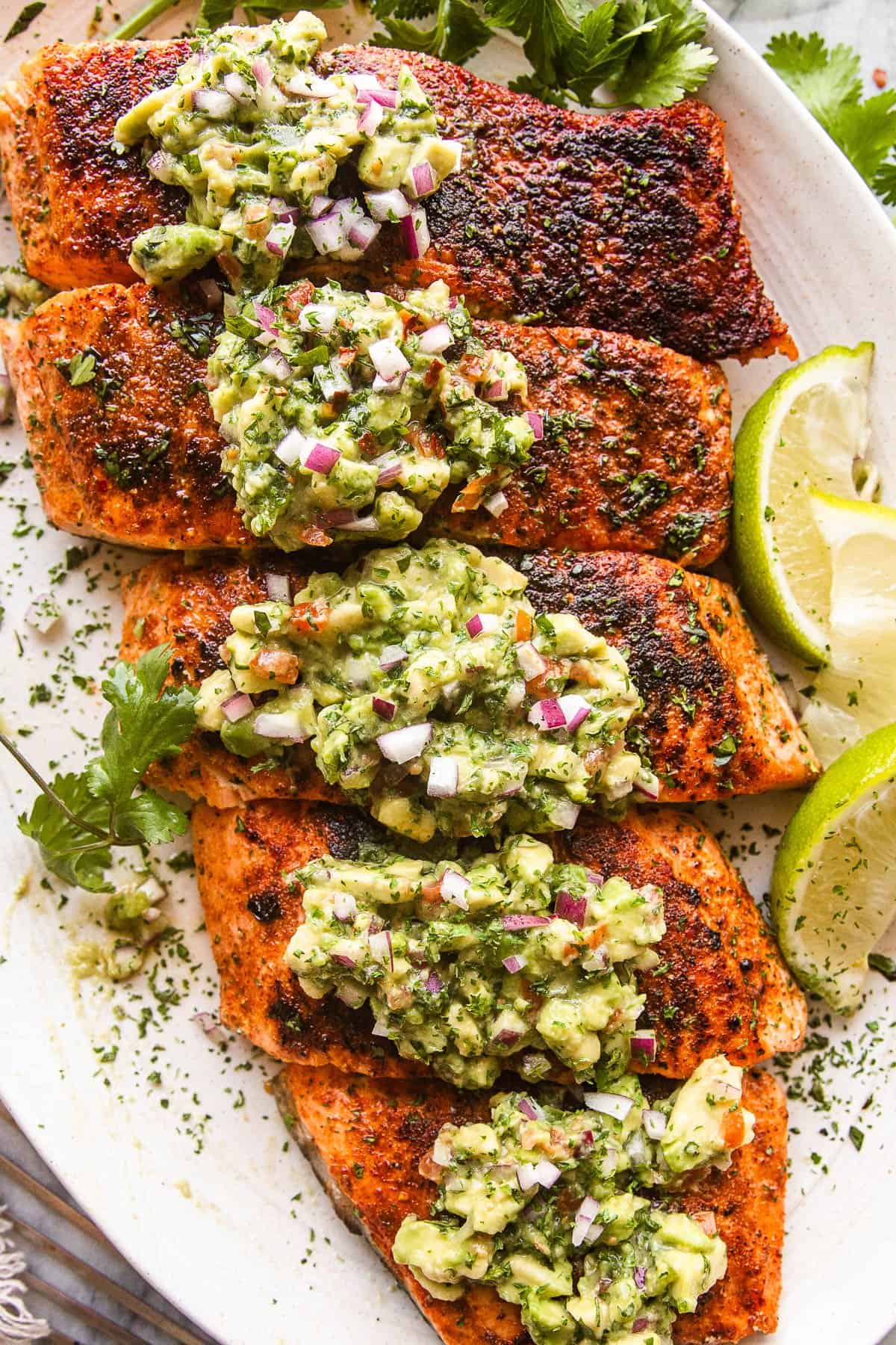 overhead shot of a large plate with grilled salmon fillets topped with avocado salsa