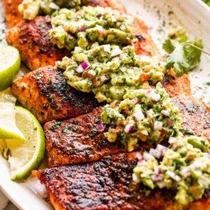 side shot of grilled salmon fillets topped with avocado salsa