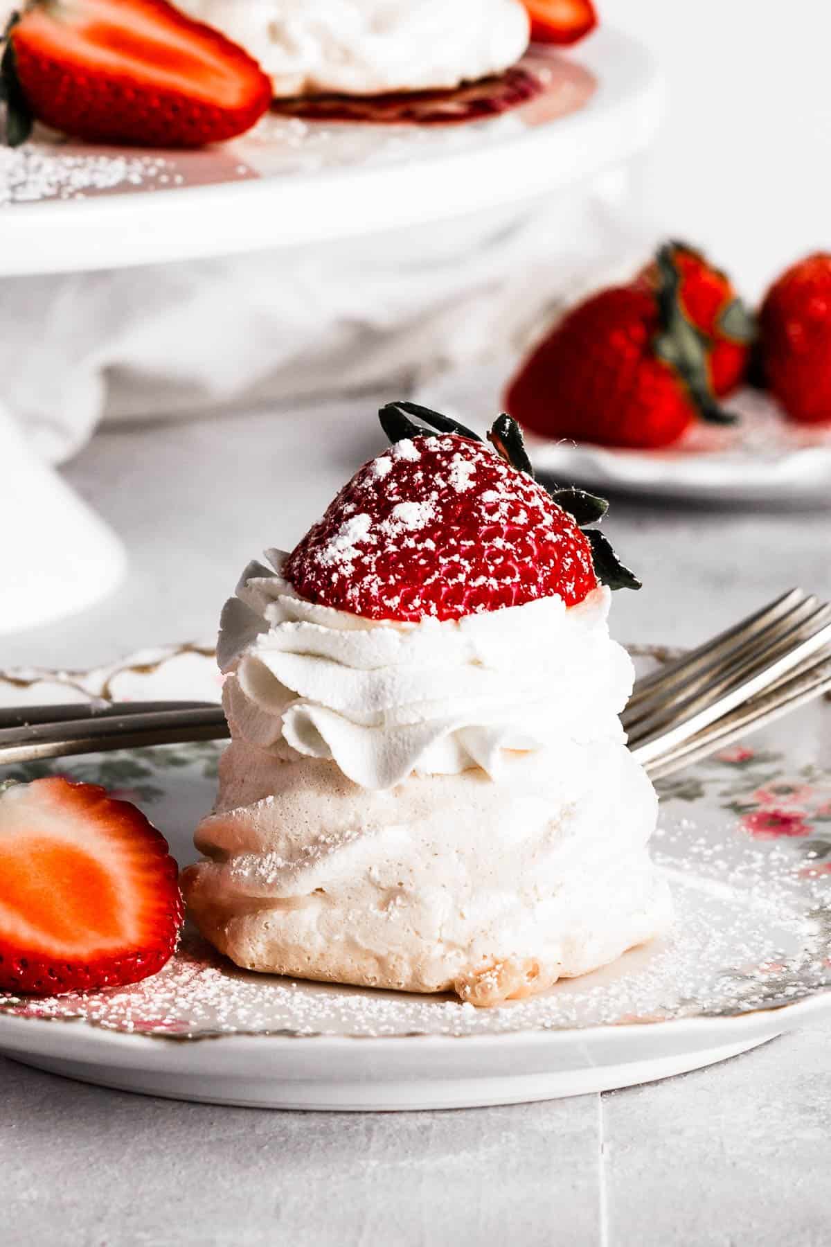 mini strawberry pavlova topped with whipped cream, strawberries, and a dust of powdered sugar