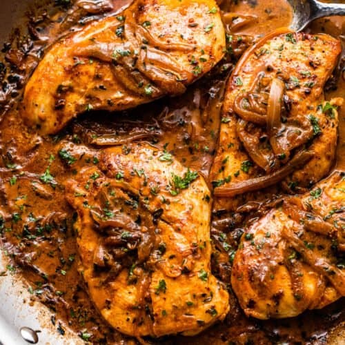 close up overhead shot of four chicken breasts cooking in a skillet with onions and gravy