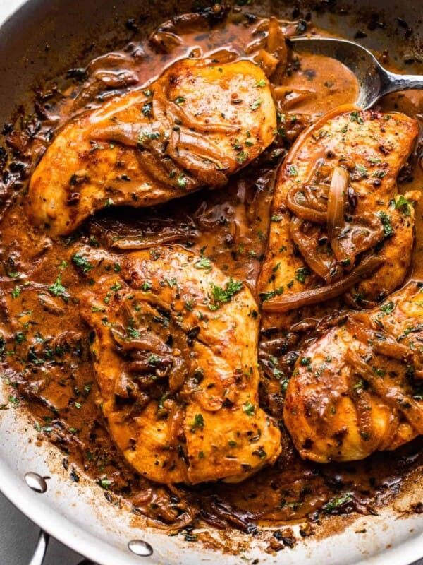 close up overhead shot of four chicken breasts cooking in a skillet with onions and gravy