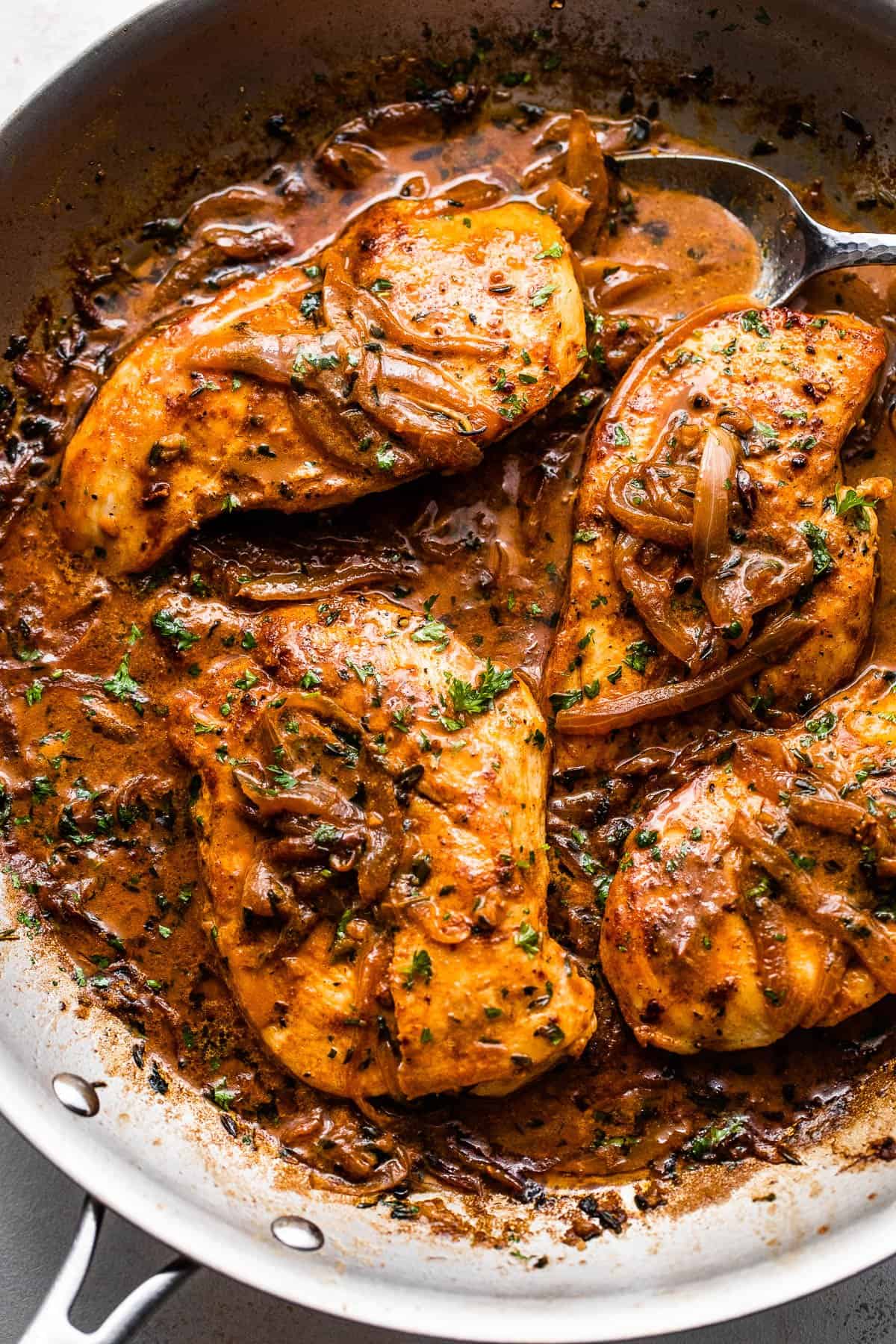 close up overhead shot of four chicken breasts cooking in a skillet with onions and gravy