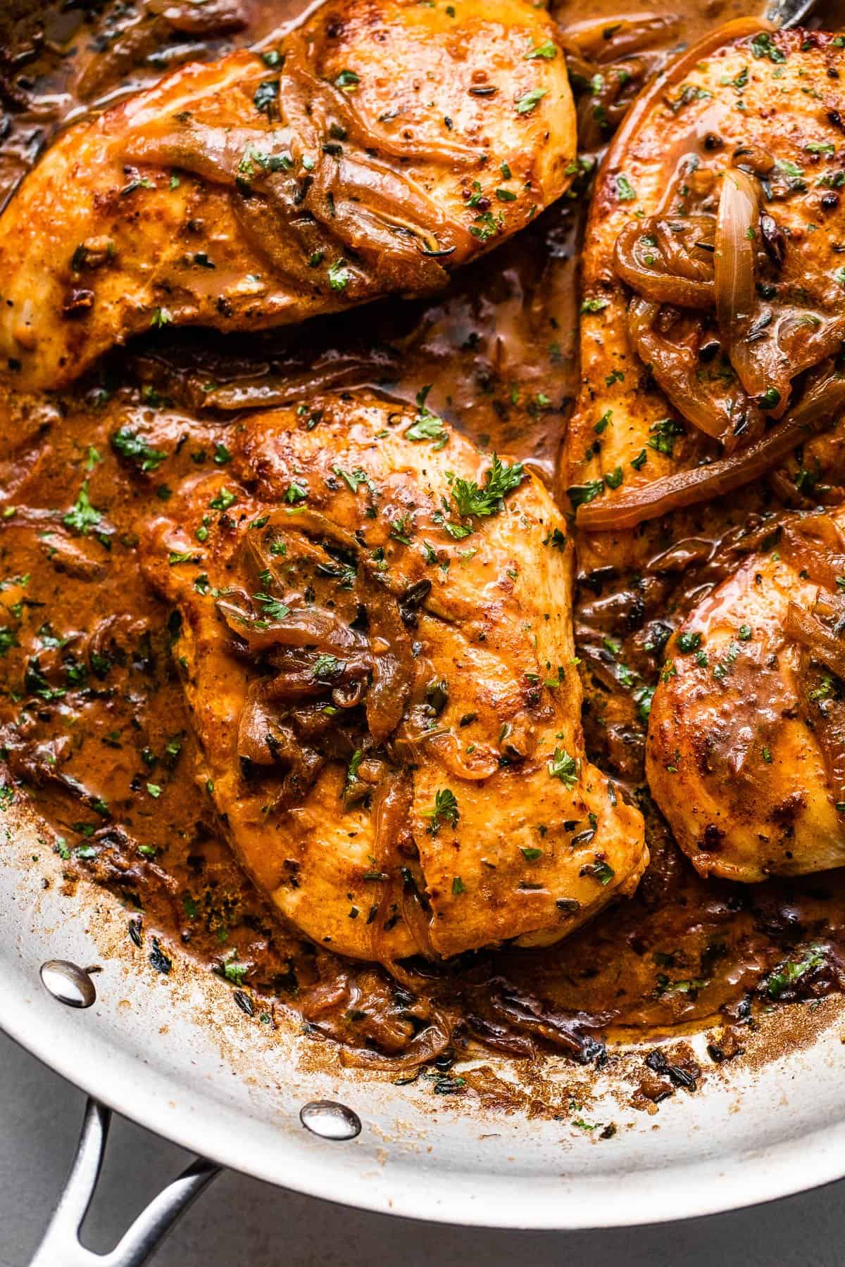 close up overhead shot of four chicken breasts cooking in a skillet with onions and gravy