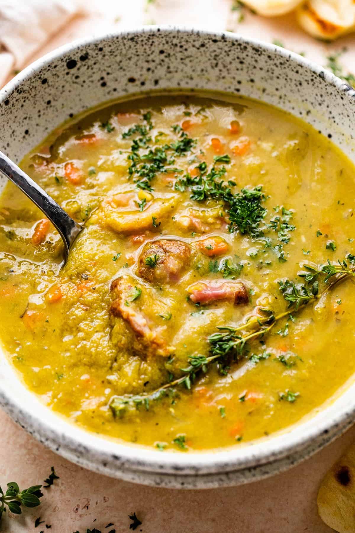 Split pea soup in a bowl with chunks of ham and herbs on top