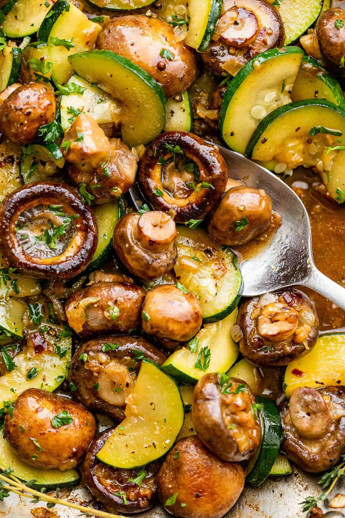 sliced zucchini and button mushrooms cooking in a stainless steel skillet