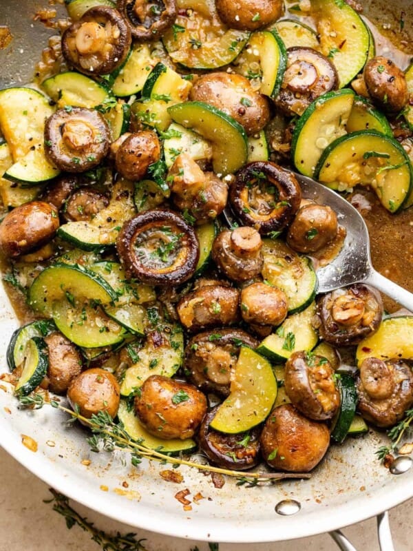 sliced zucchini and button mushrooms cooking in a stainless steel skillet