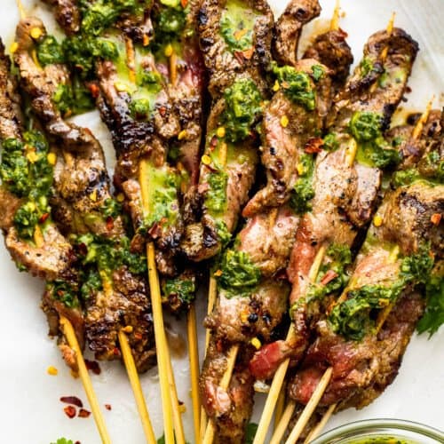 eight Grilled Steak Skewers served on a plate and topped with chimichurri sauce