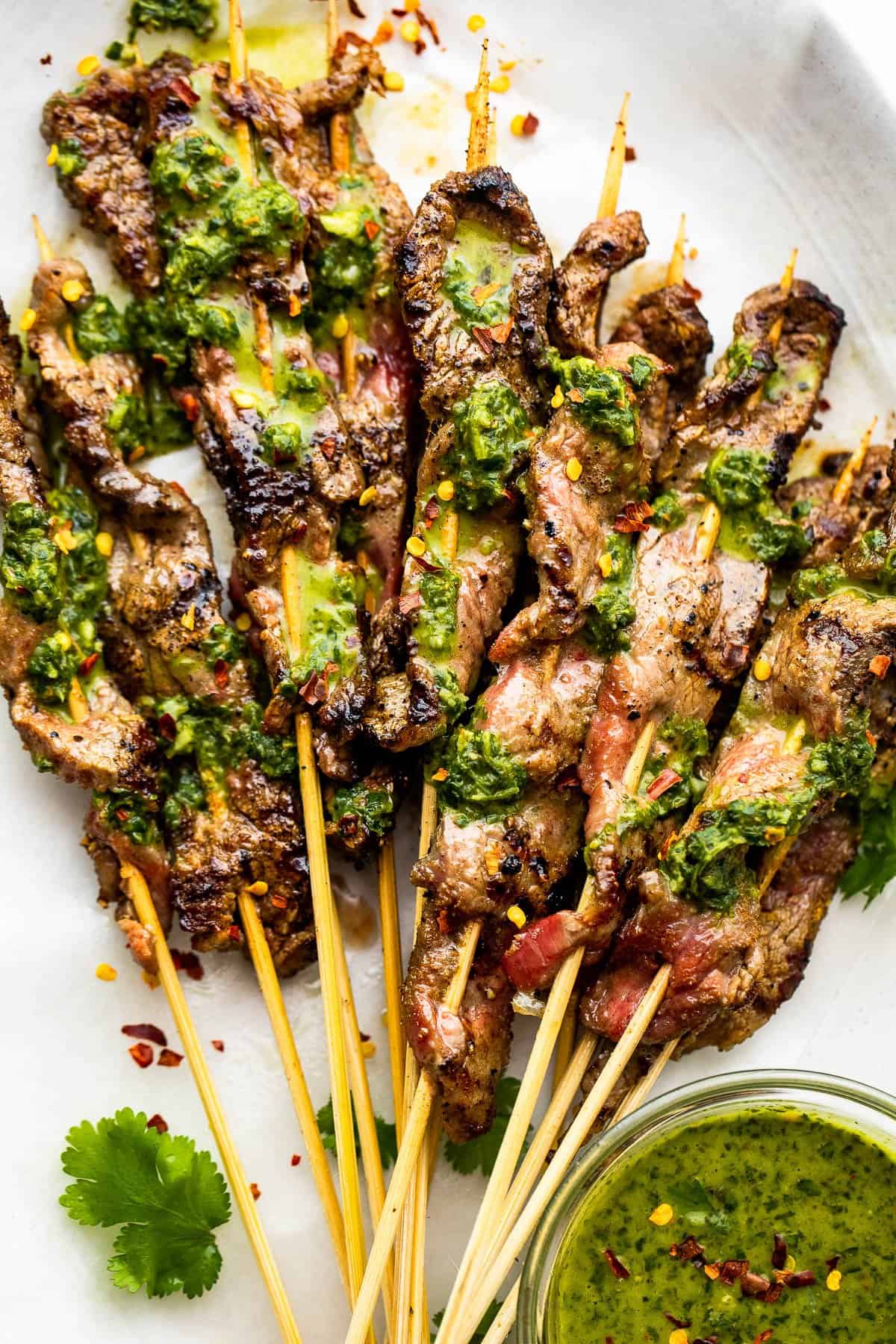 eight Grilled Steak Skewers served on a plate and topped with chimichurri sauce