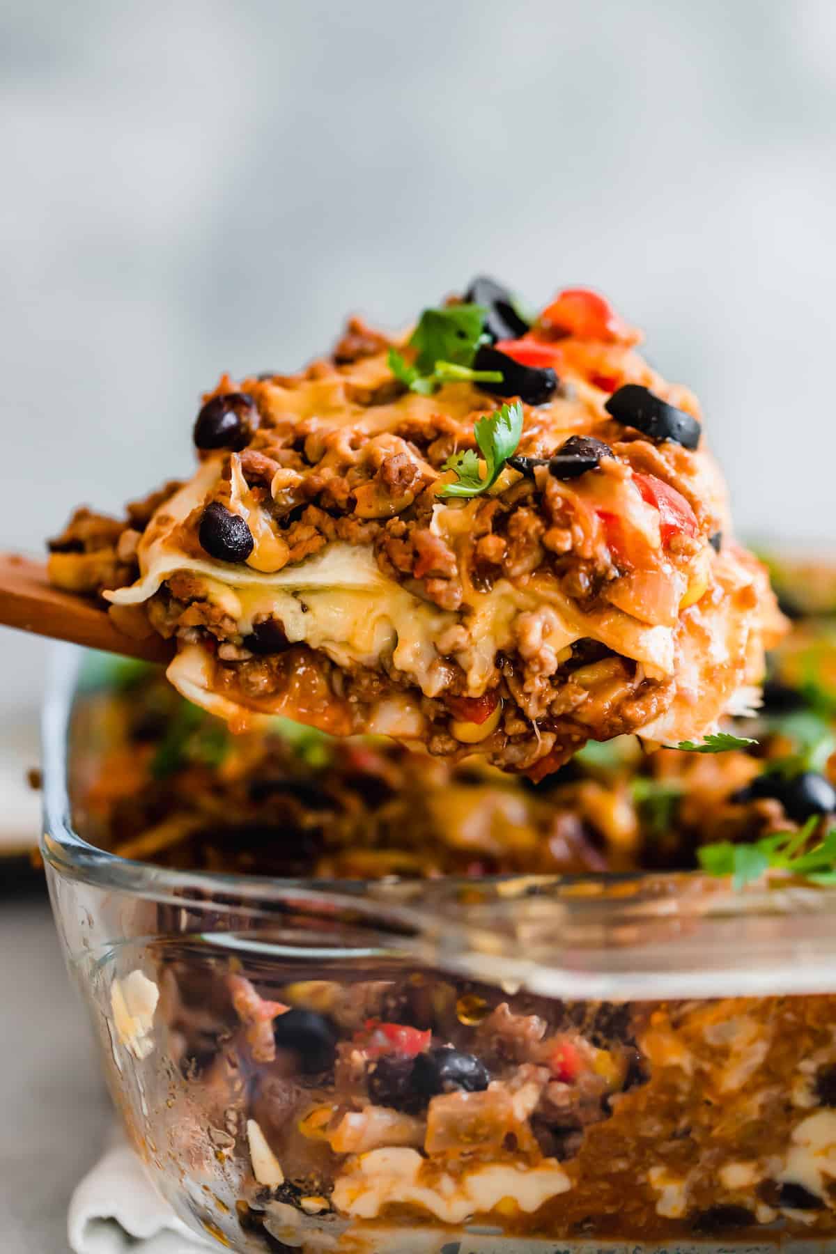 scooping out mexican lasagna from a casserole dish.