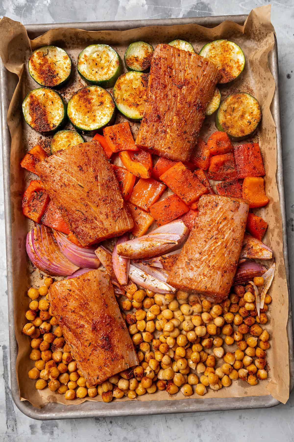 Overhead view of seasoned mahi mahi filets arranged on a sheet pan with chickpeas and vegetables.