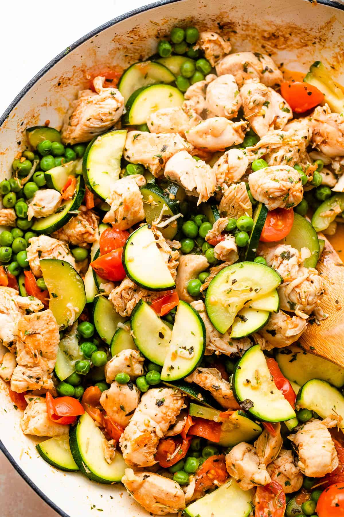 Chicken bites, zucchini slices, peas, and tomatoes cooking in a skillet.