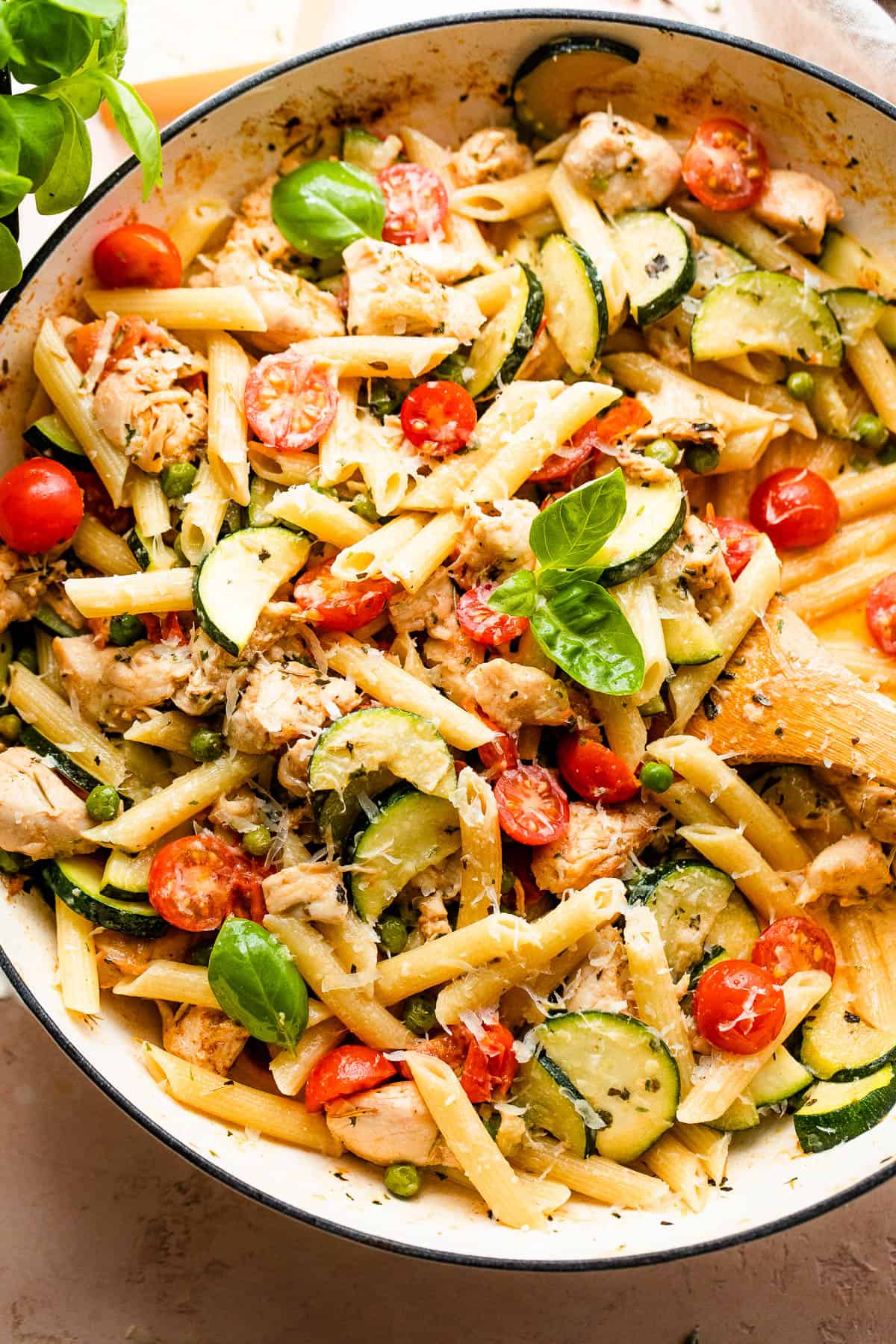 Cooked penne pasta, bites of chicken, and vegetables in a skillet.