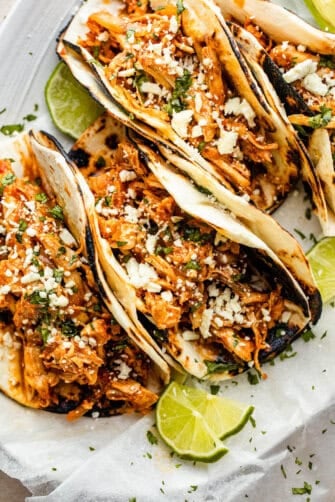 four chicken tinga tacos arranged on a plate and topped with cheese