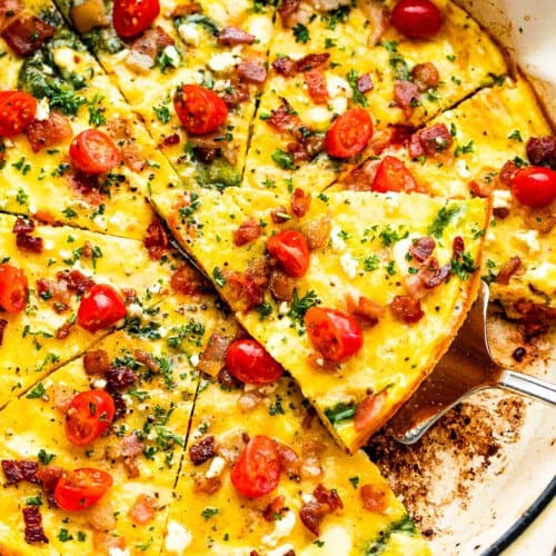 overhead shot of a sliced frittata in a white skillet topped with bacon and tomatoes