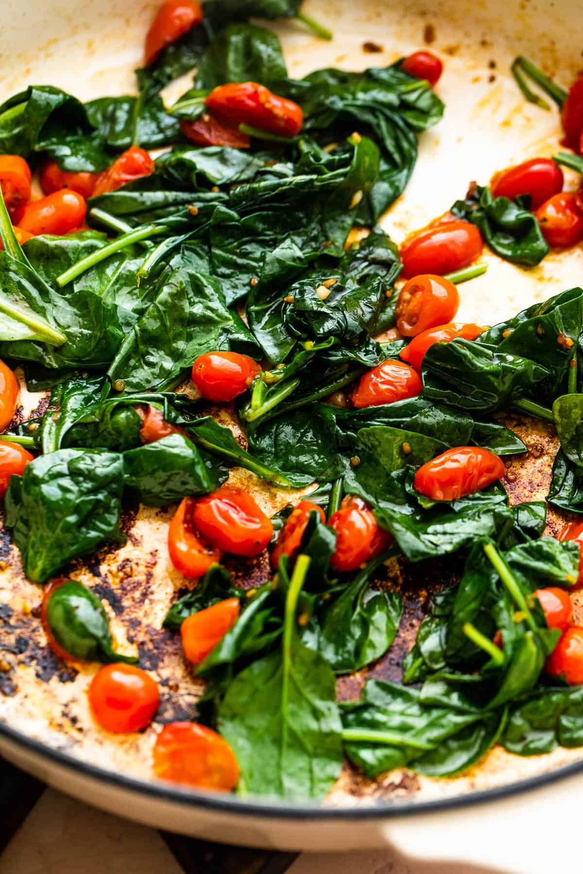 cooking spinach and cherry tomatoes in a white heavy bottomed skillet