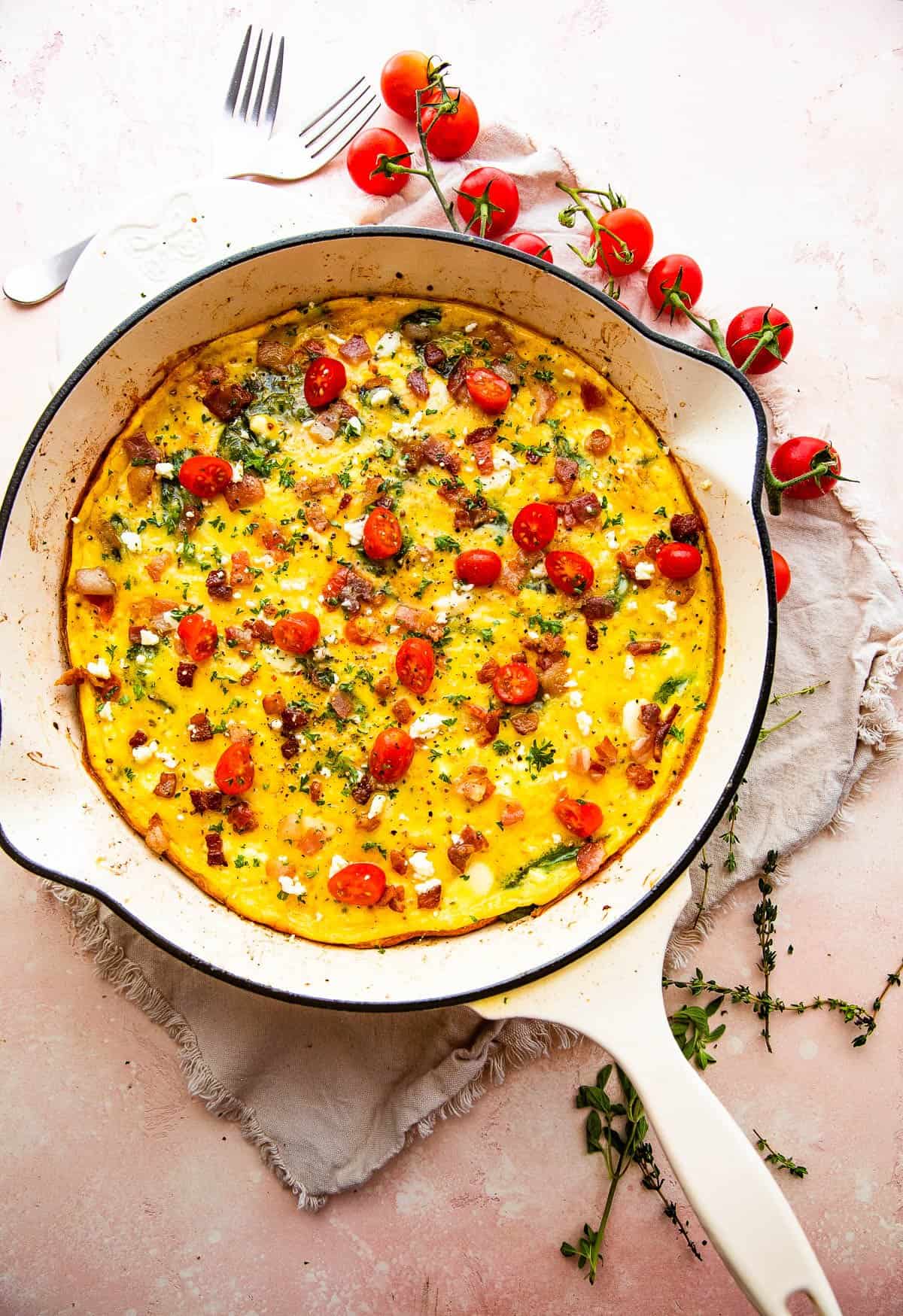 overhead shot of a frittata in a white skillet topped with bacon and tomatoes