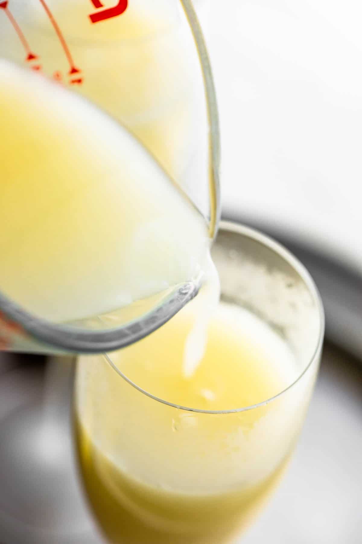 This pineapple mimosa tastes like a bubbly Dole Whip! It's made with coconut milk, pineapple juice, and prosecco. It's perfect for summer. pouring pineapple and coconut milk in a champagne flute
