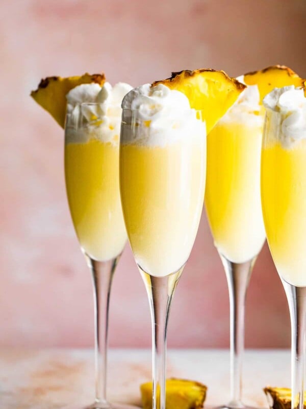 four champagne flutes filled with pineapple dole whip mimosas and topped with whipped cream and pineapple slices