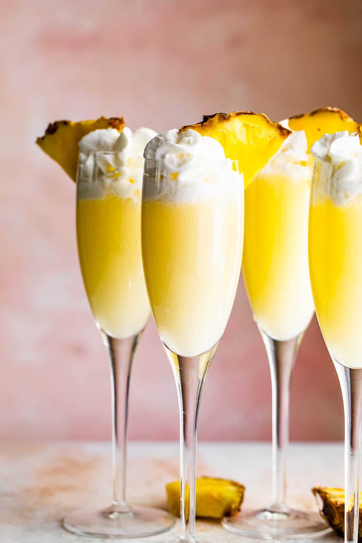four champagne flutes filled with pineapple dole whip mimosas and topped with whipped cream and pineapple slices