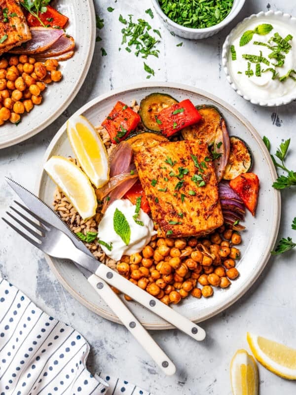 Two dinner plates with Mahi mahi filet served with crispy chickpeas, roasted vegetables, and Greek yogurt on a plate.