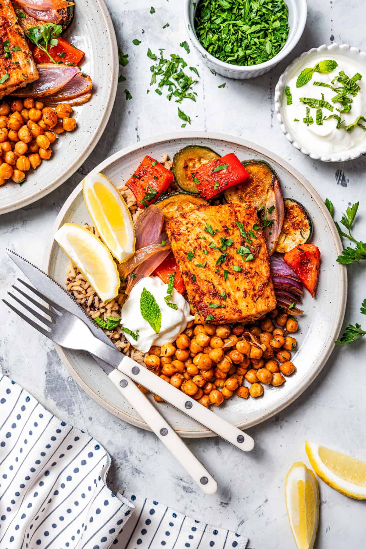Two dinner plates with Mahi mahi filet served with crispy chickpeas, roasted vegetables, and Greek yogurt on a plate.