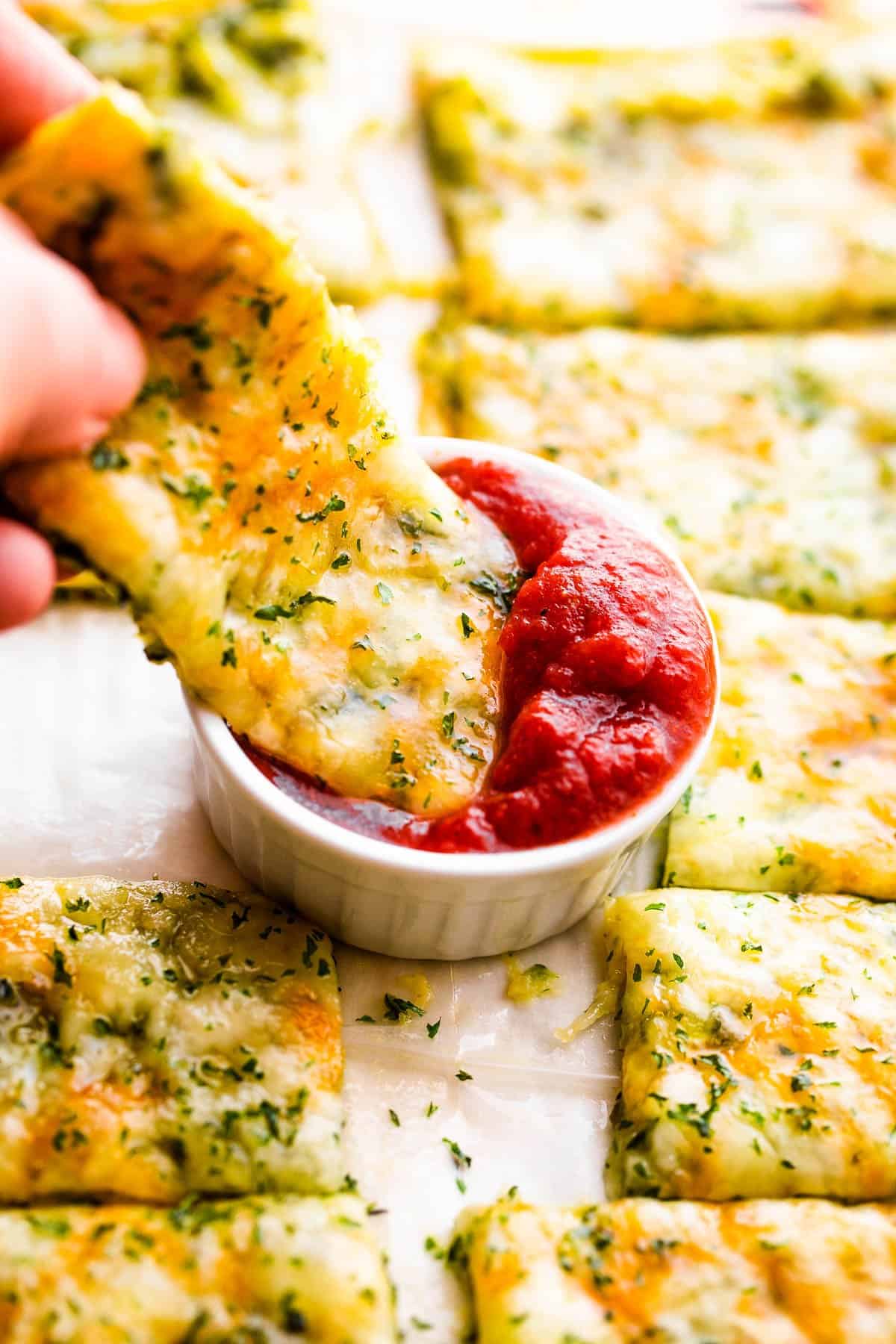 dipping cheesy zucchini breadsticks in marinara sauce