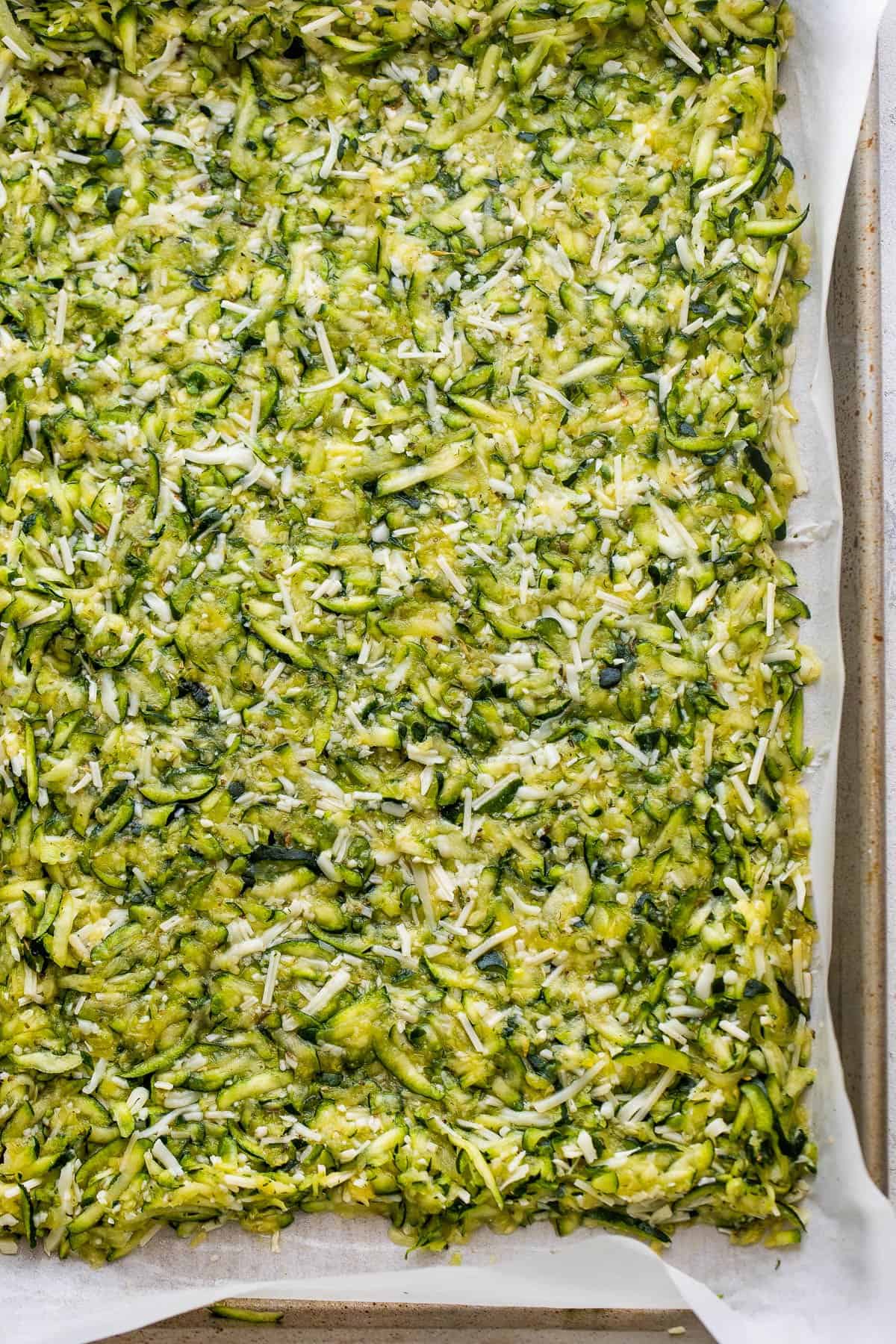 shredded zucchini and cheese mixture on the bottom of a baking dish lined with parchment paper