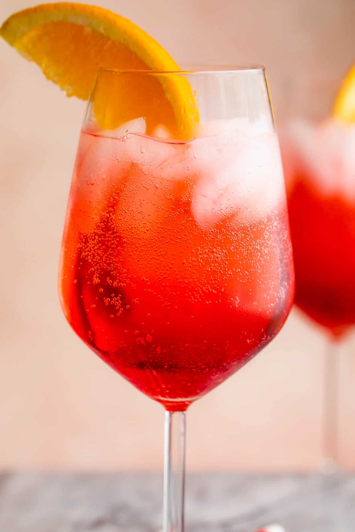 close up shot of Campari Spritz in a tall stemmed glass served with a slice of orange on the rim and red and white straw
