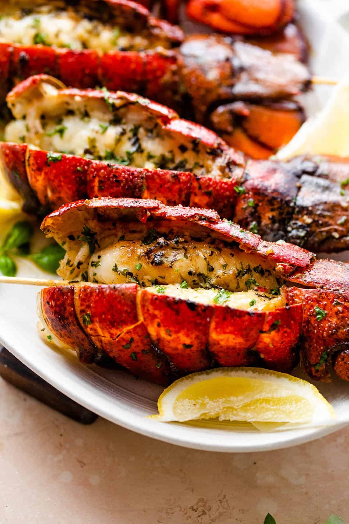 side shot of four grilled lobsters on a plate with lemon wedges