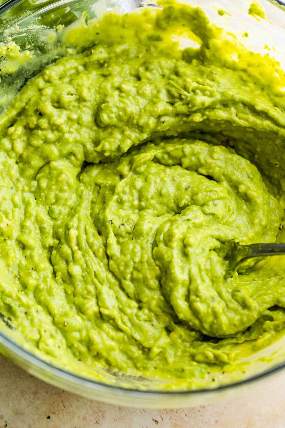 Made with juicy mango, garlic, jalapeño, and crisp bell peppers, this easy guacamole recipe is packed with irresistible flavor and texture! Mashed avocado in a large glass bowl.