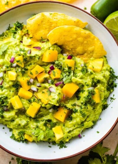 bowl of guacamole studded with mango chunks and two tortilla chips