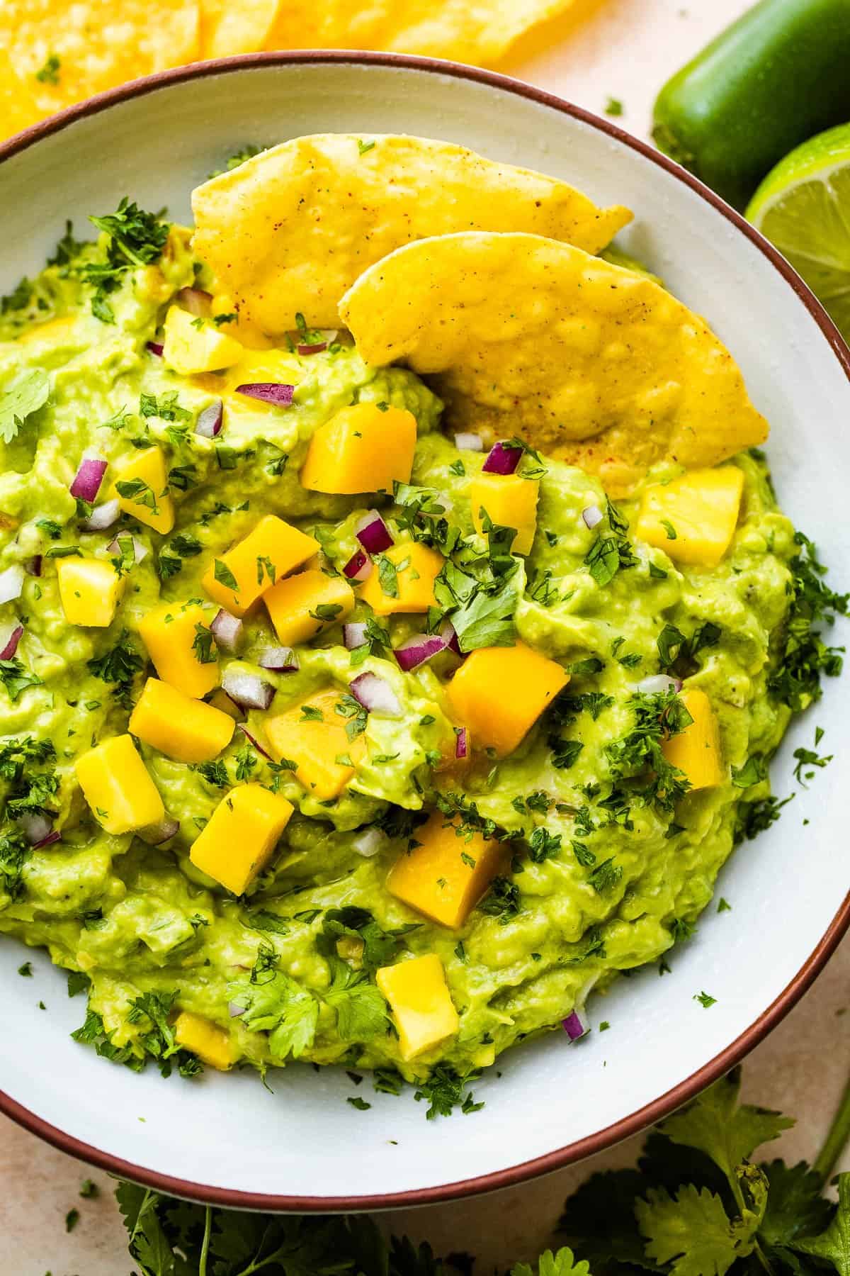 bowl of guacamole studded with mango chunks and two tortilla chips