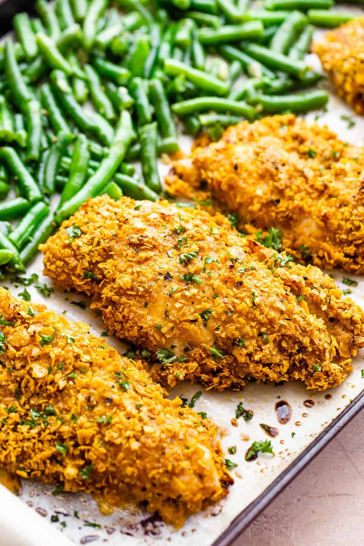 side shot of a baking sheet with four breaded chicken breasts and green beans