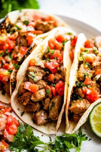 side shot of three pork carnitas tacos topped with tomatoes, cilantro, and onions