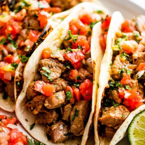 side shot of three pork carnitas tacos topped with tomatoes, cilantro, and onions