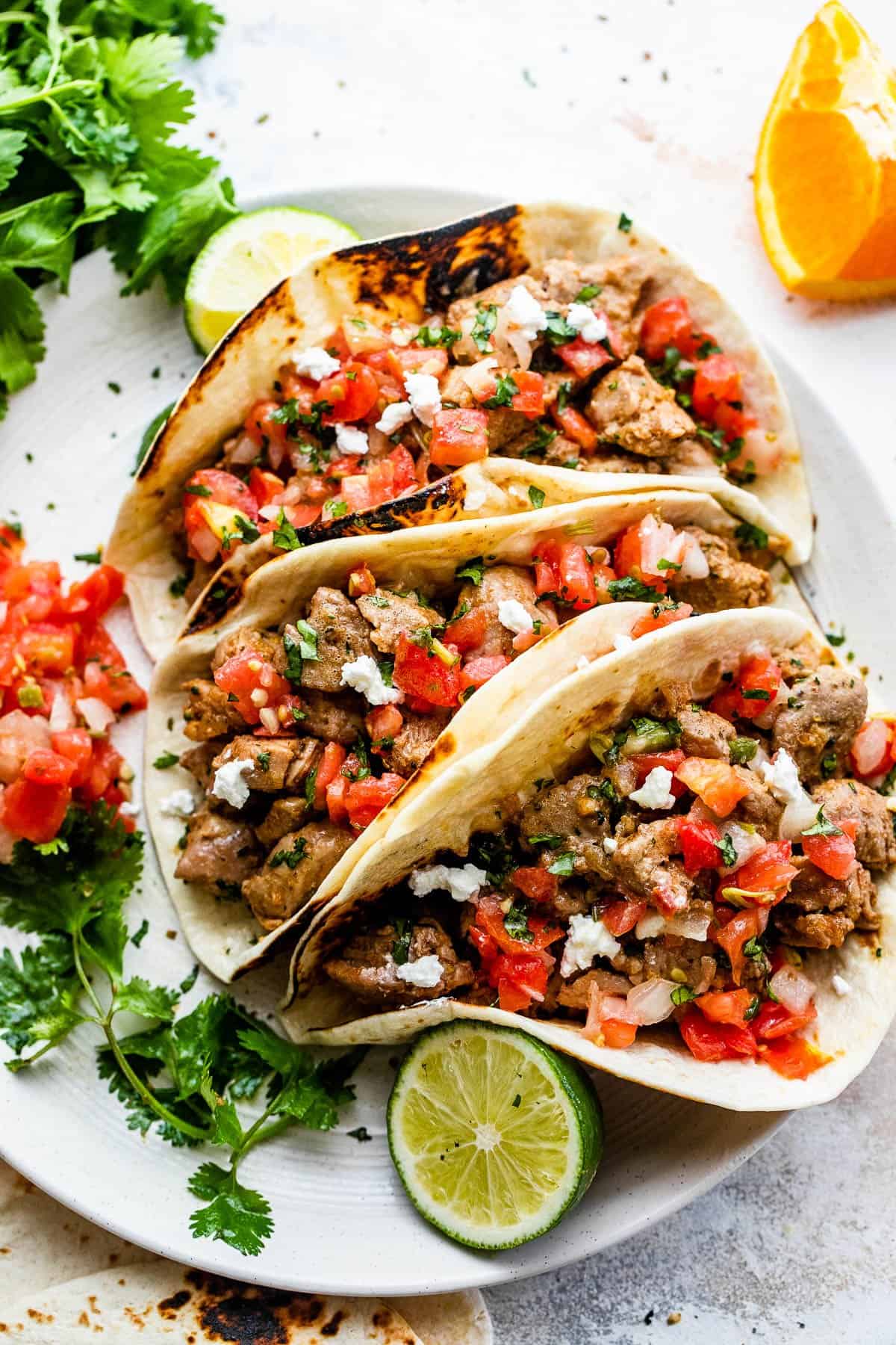 overhead shot of three pork carnitas tacos served on a round plate with pico de gallo