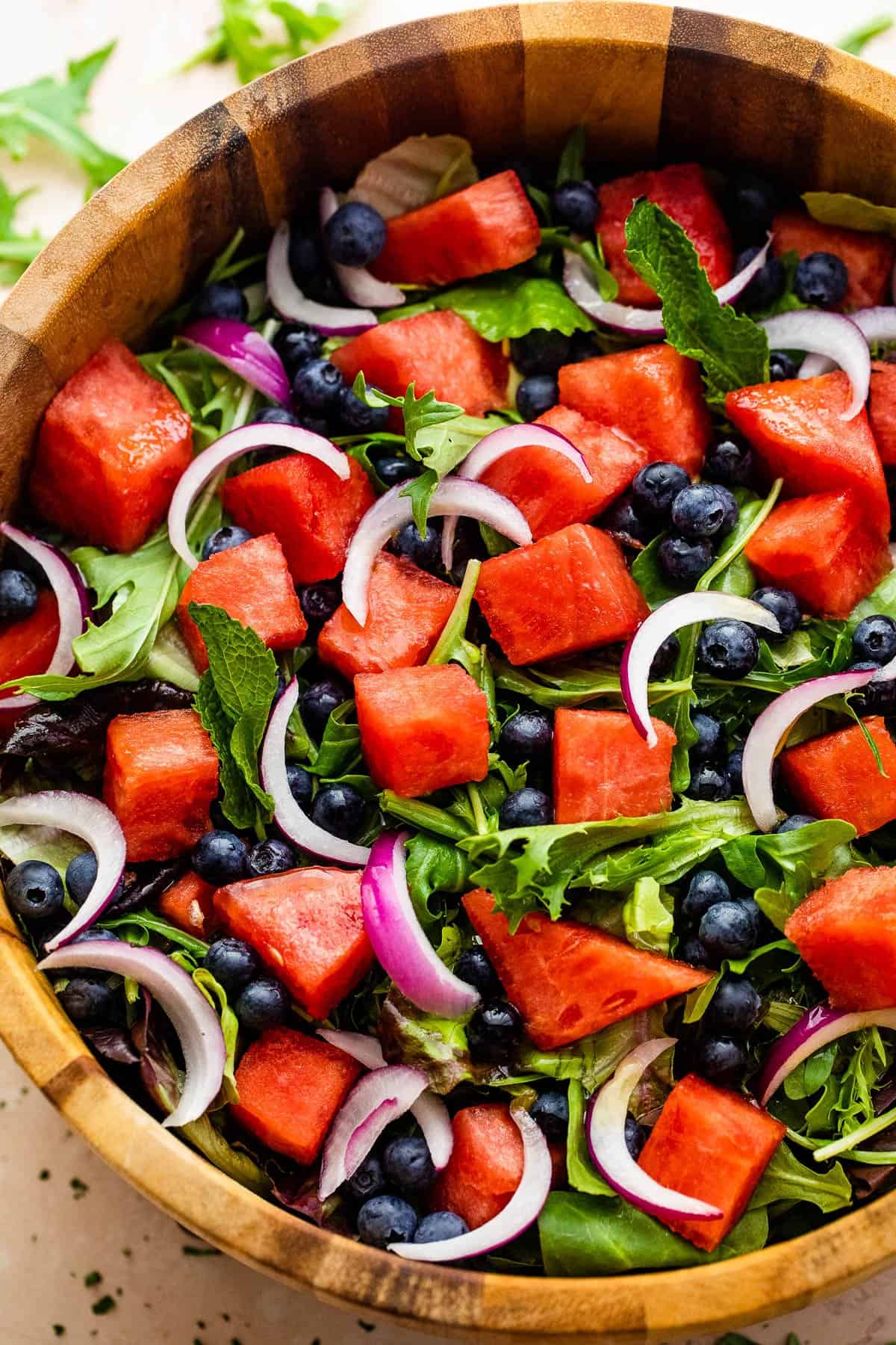 cubed watermelon, blueberries, and sliced red onions atop a bed of torn up lettuce greens in a salad bowl