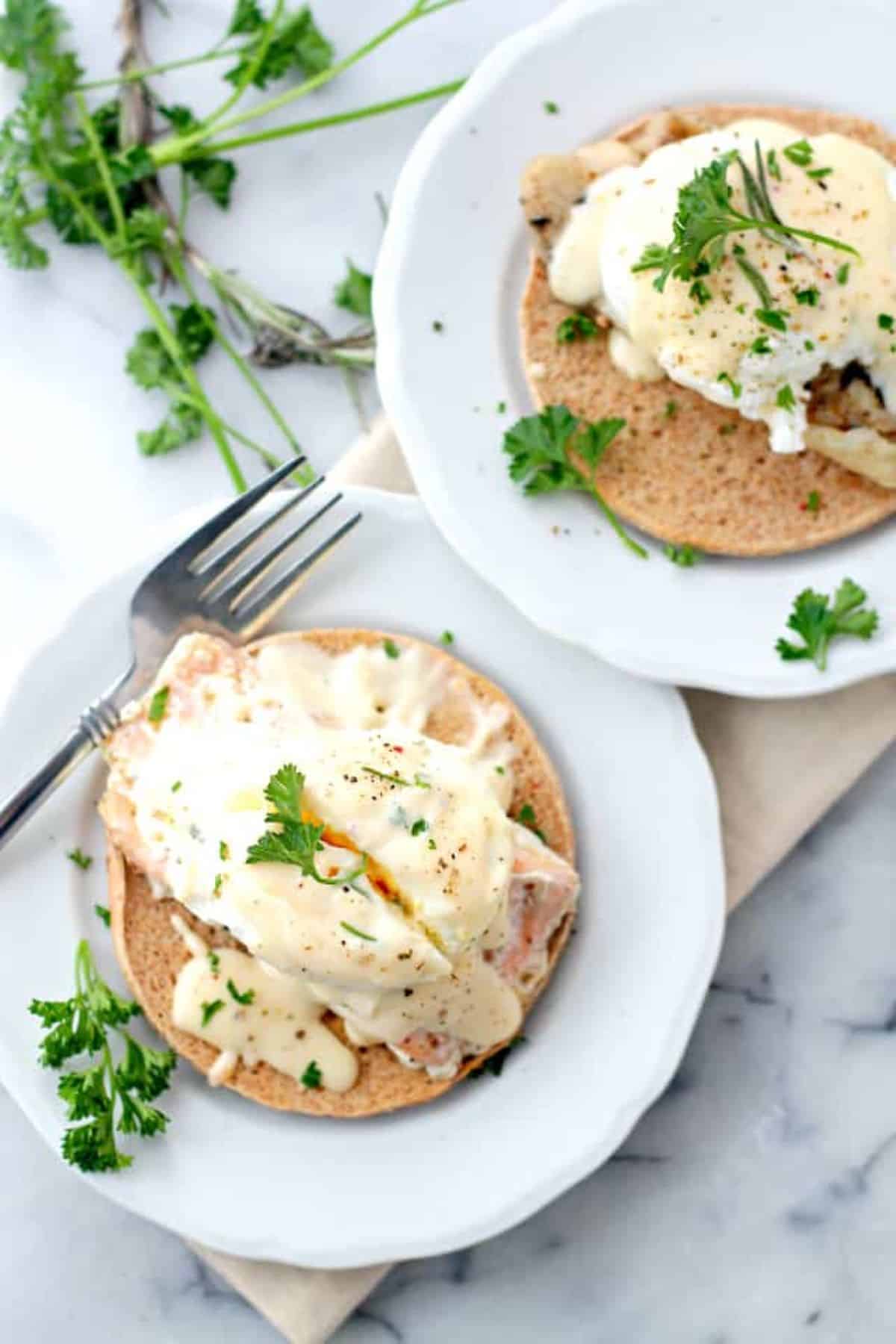Two servings of poached-egg salmon with cheese sauce on white plates, garnished with parsley.