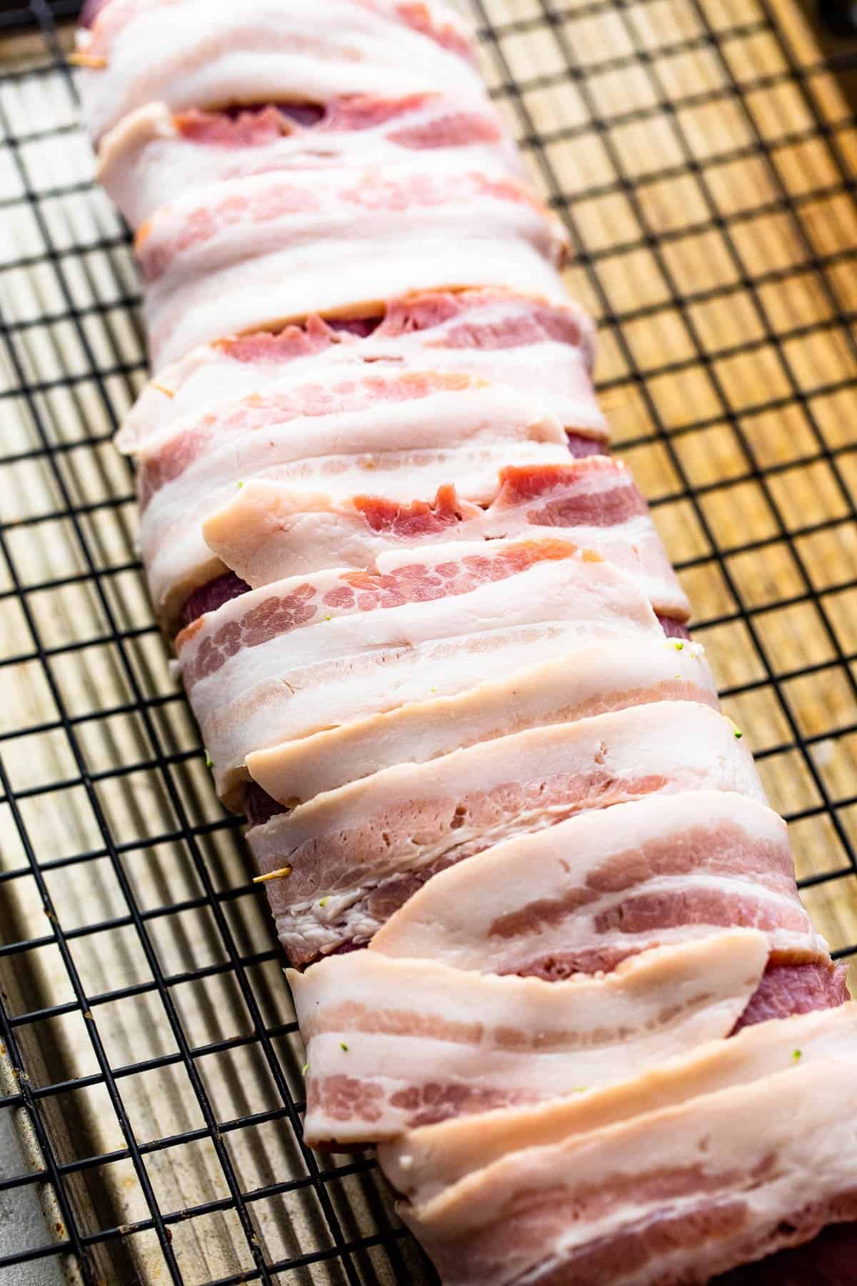 raw pork tenderloin wrapped in pork and set on a wire rack