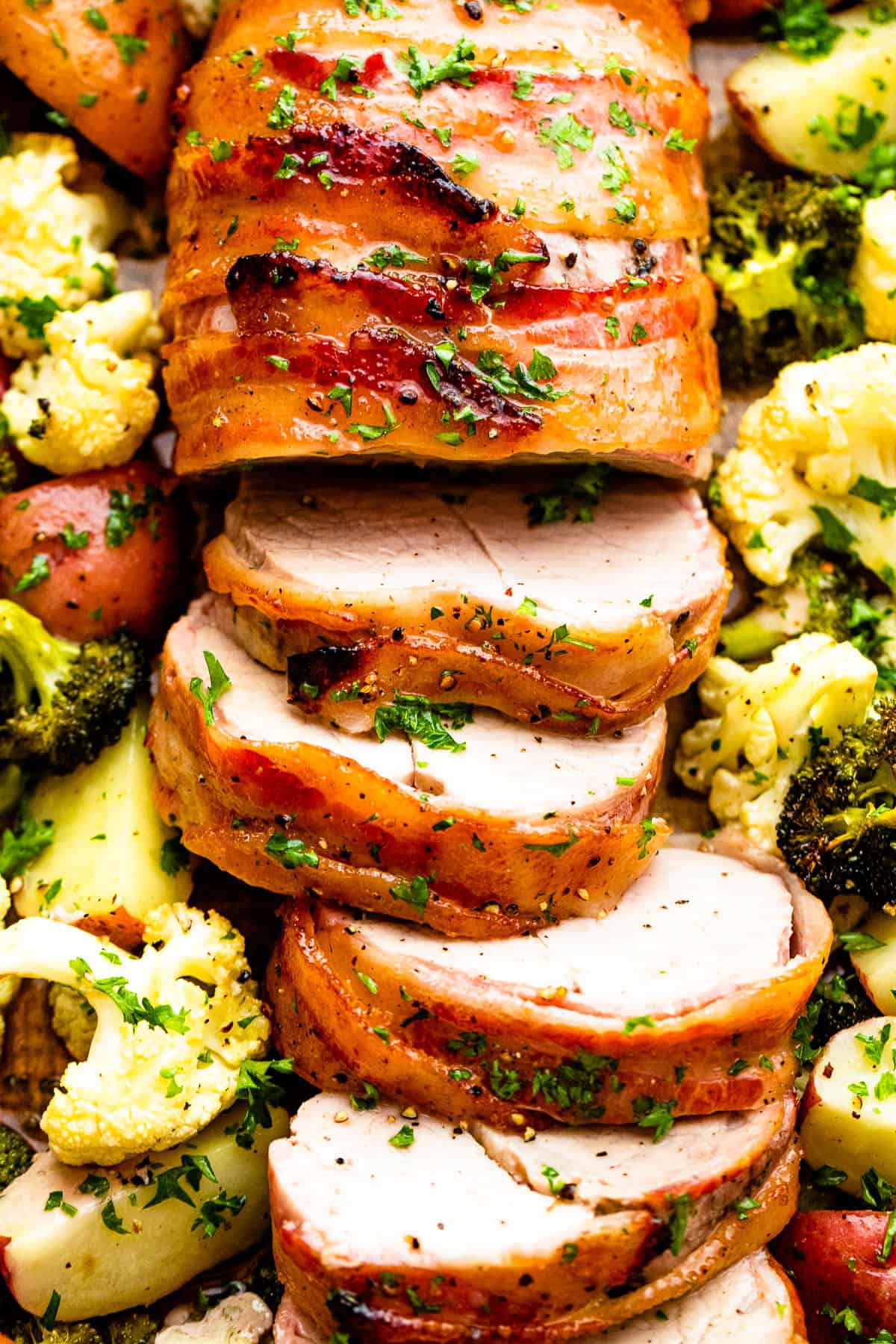 roasted pork tenderloin wrapped in bacon and vegetables spread around it