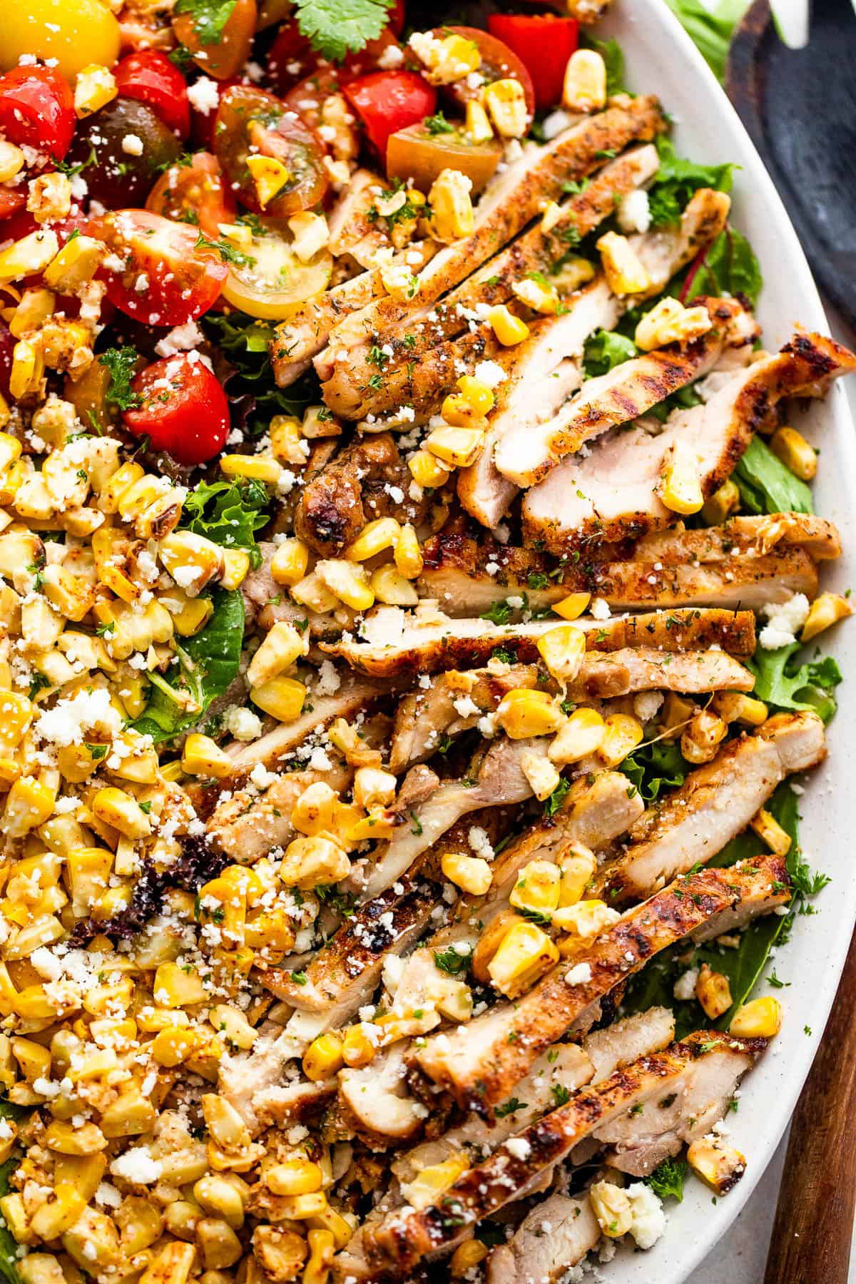 slices of chicken thighs on a bed of lettuce with halved cherry tomatoes, corn kernels, and cotija cheese