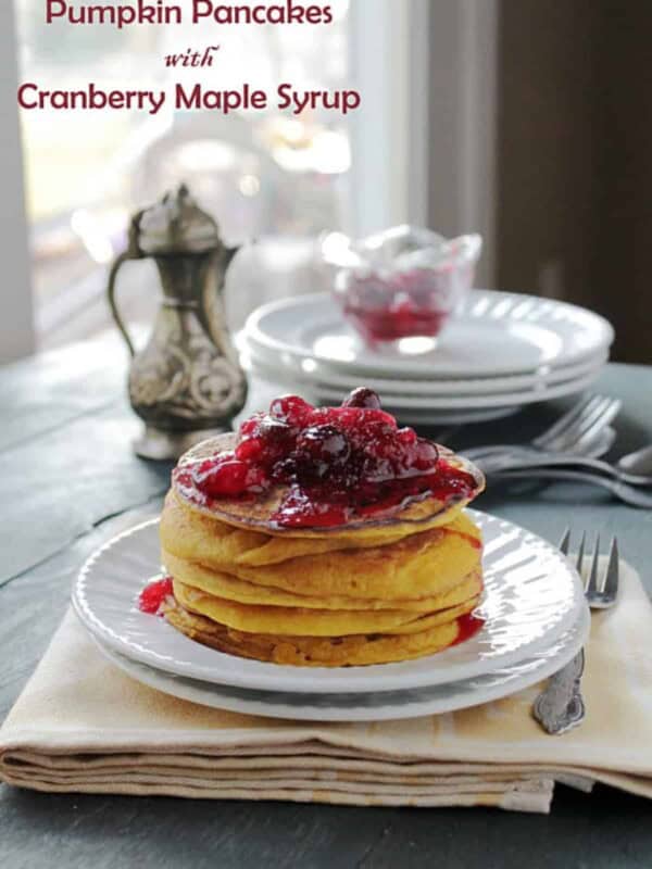 A stack of pumpkin pancakes topped with cranberry maple syrup on a white plate.