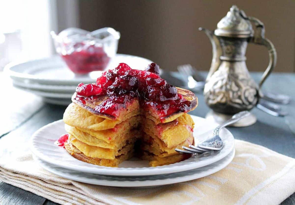 A stack of pancakes topped with cranberry maple syrup, with a bite cut out.