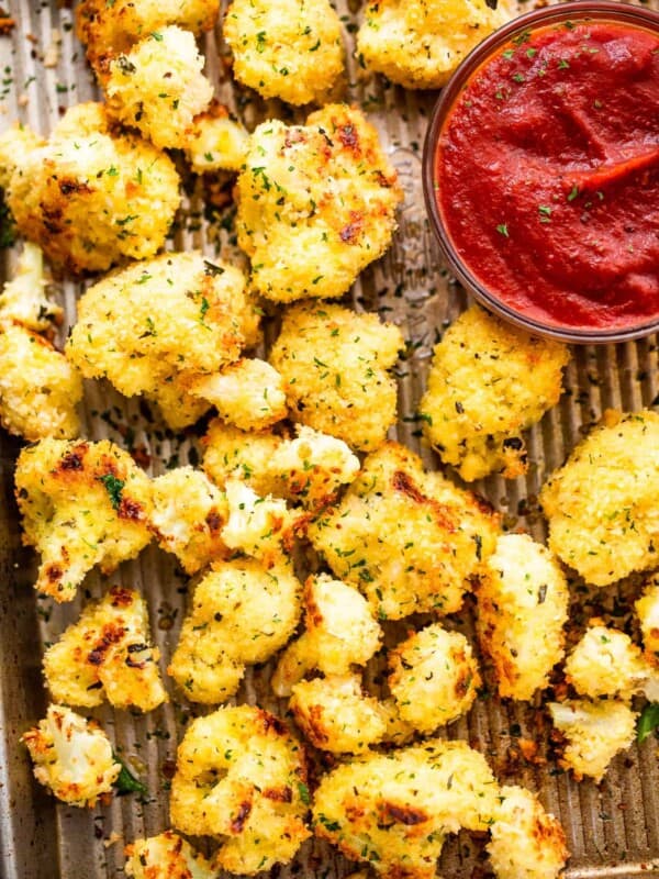 baked parmesan cauliflower bites arranged on a baking sheet and a bowl of marinara sauce set next to them