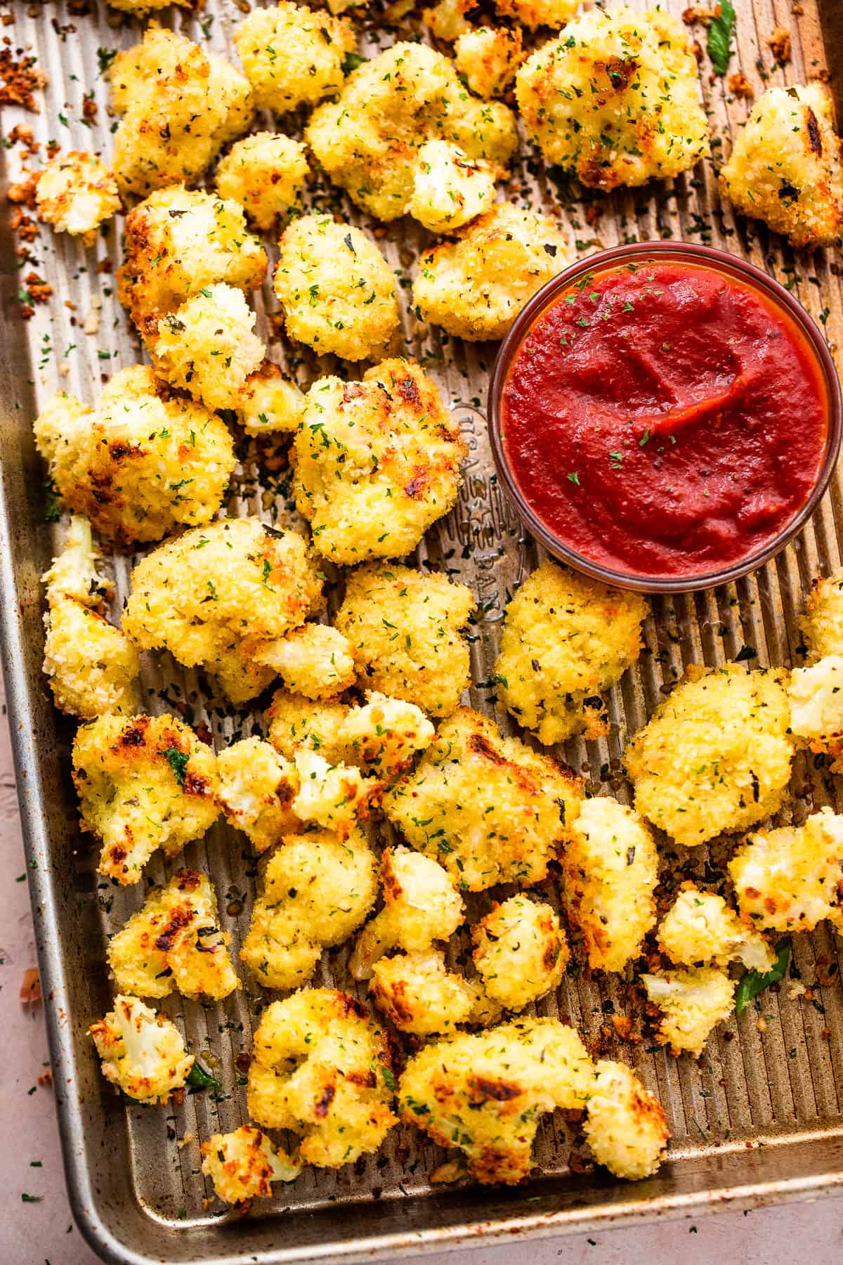 baked parmesan cauliflower bites arranged on a baking sheet and a bowl of marinara sauce set next to them